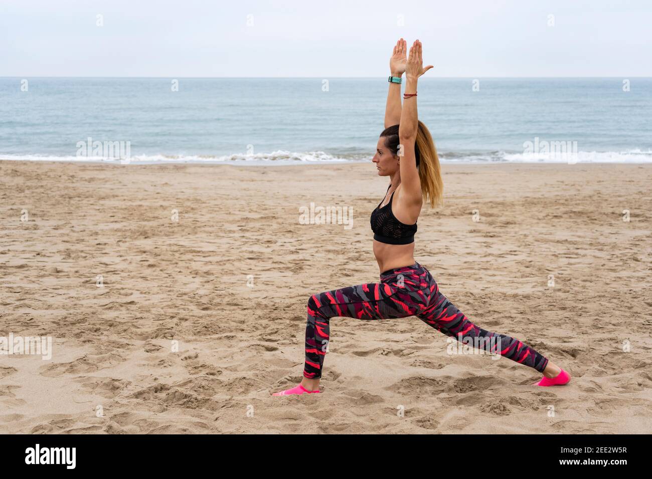 Young fit attractive female practicing yoga warrior one pose , Virabhadrasana posture.Athletic woman working out outdoors, at the beach seaside , life Stock Photo