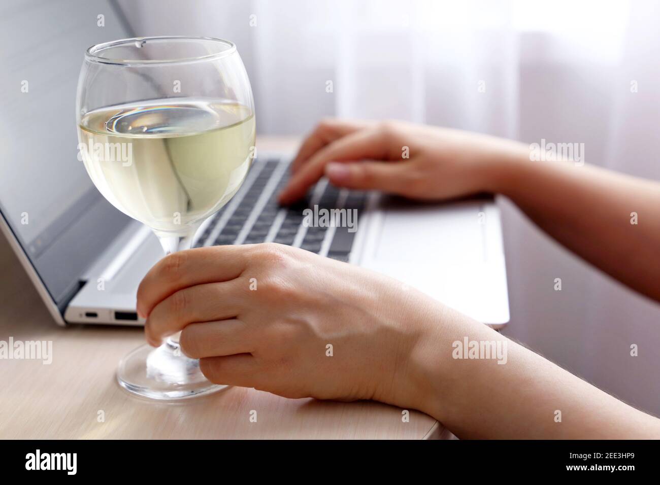 Glass of white wine in female hand, woman using laptop and drinking alcohol. Remote work and relax during quarantine at home Stock Photo