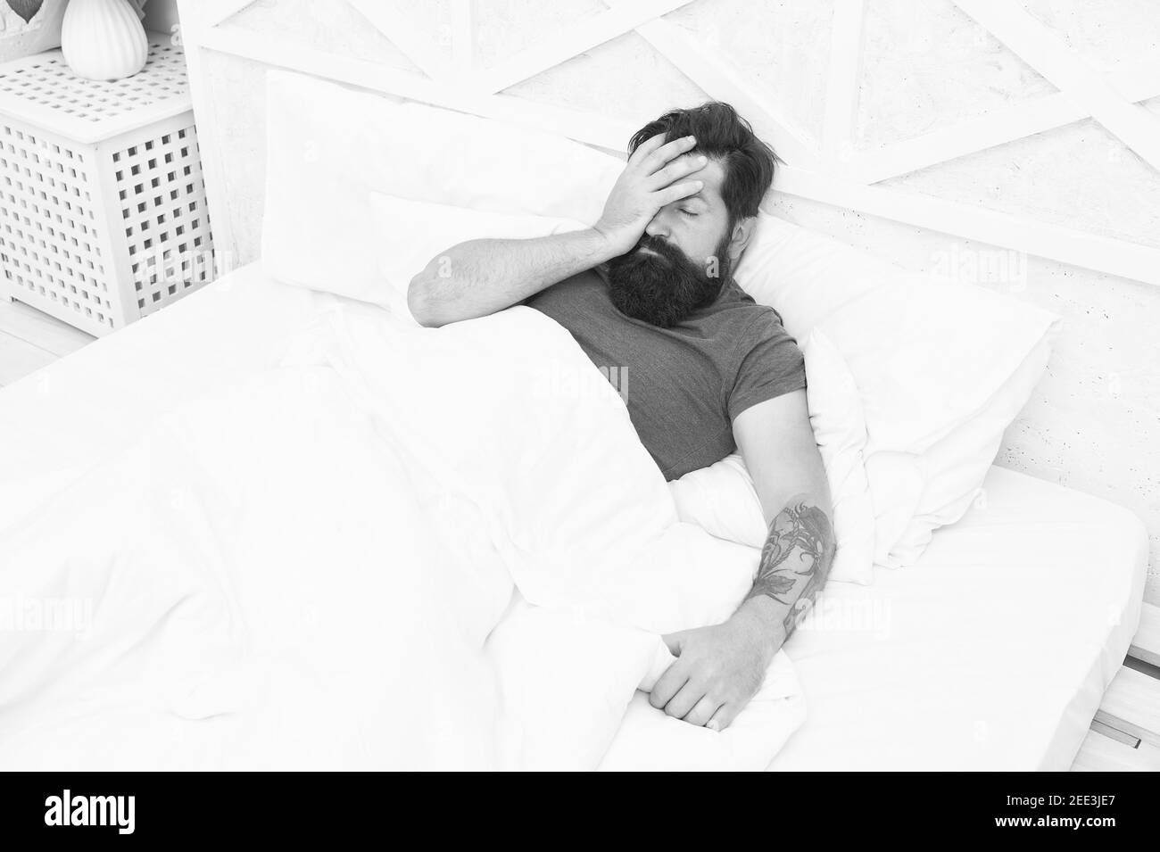 oh no. bachelor has hangover. guy at bedroom. lazy sunday. bed time routine. brutal male wake up with headache. relax lifestyle concept. tired bearded man in bed. early wake up at morning. Stock Photo