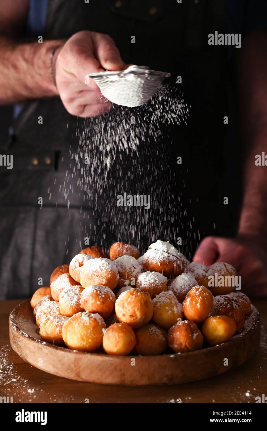 Man sprinkles powdered sugar onBaked castagnole. Street food, round