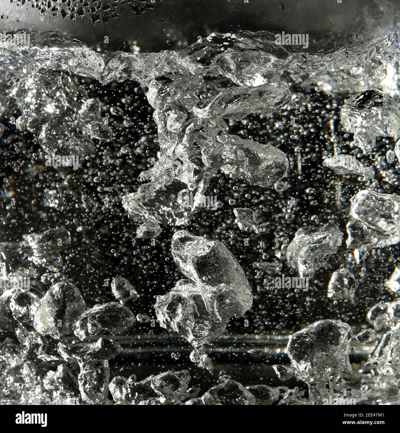 Bubbles form in boiling water in a glass kettle on a black background