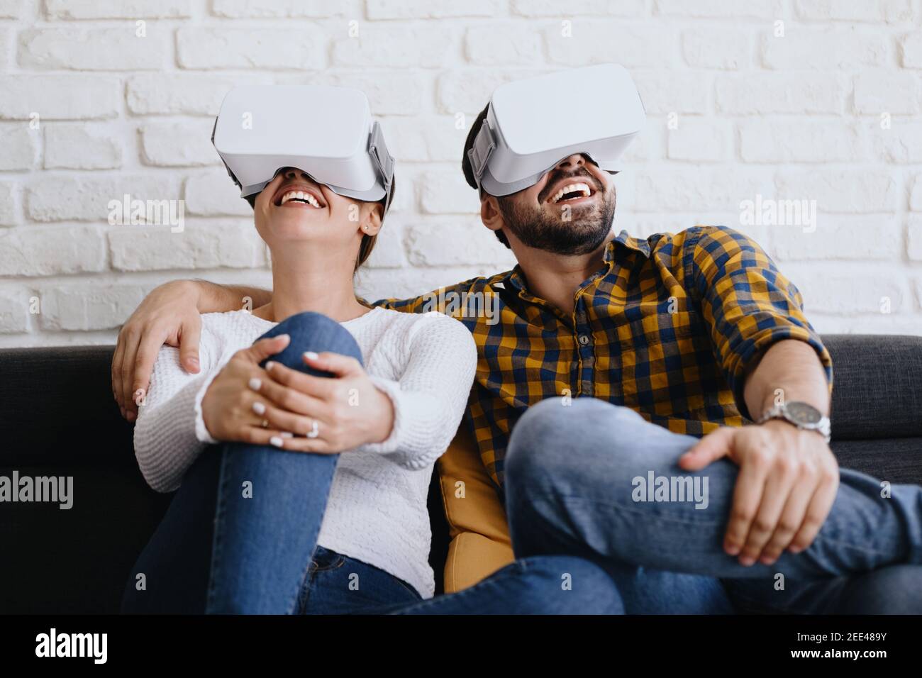 Young Couple Playing Virtual Reality With Headset On Sofa Stock Photo