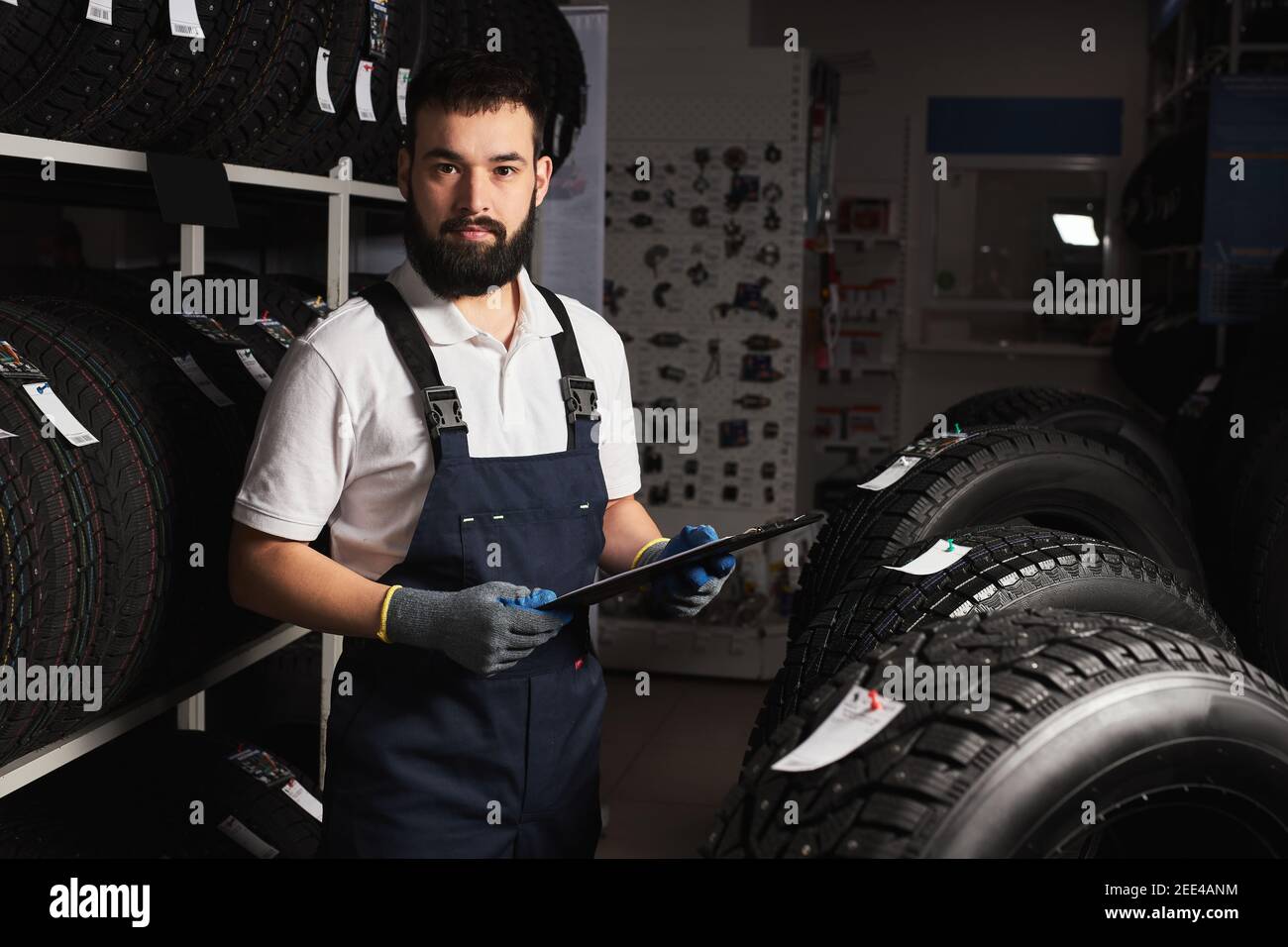 male mechanic near rack with car tires in auto store, looking at camera ...