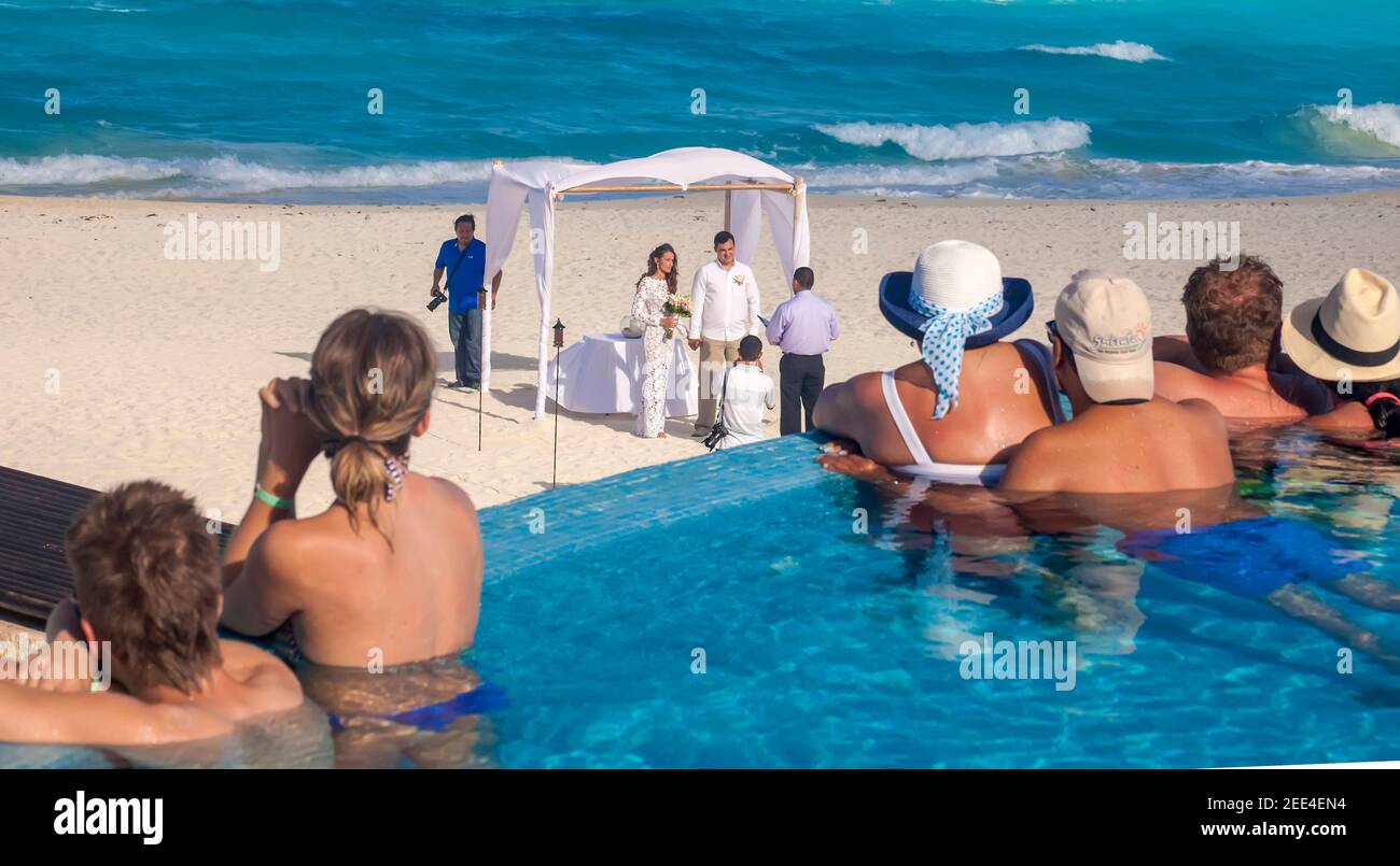 People in pool look on at a couple in a romantic ceremony and photographers on beach Cancun, Quintana Roo, Mexico Stock Photo