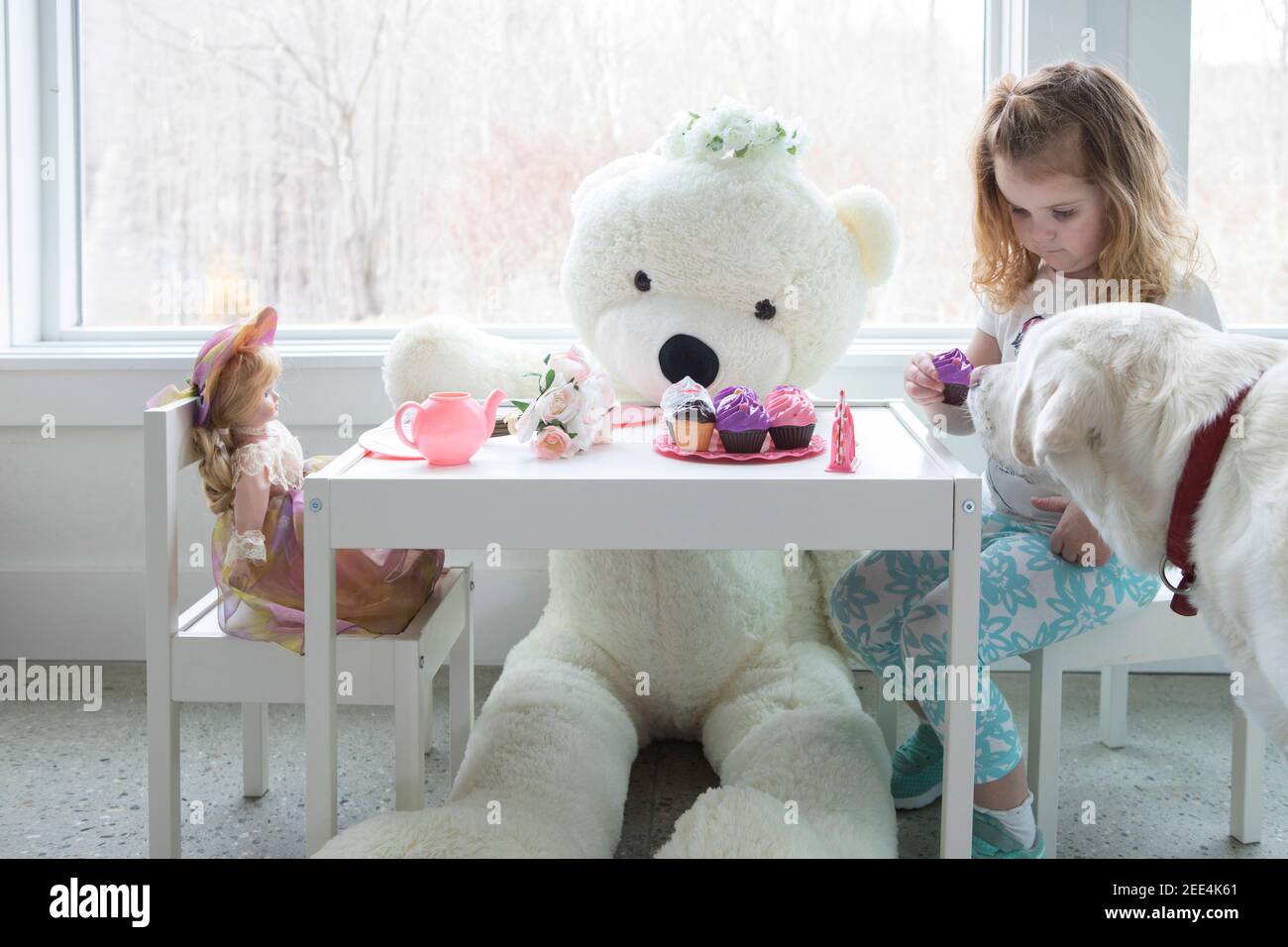 A little girl having a pretend tea party with her dog and toys. Stock Photo