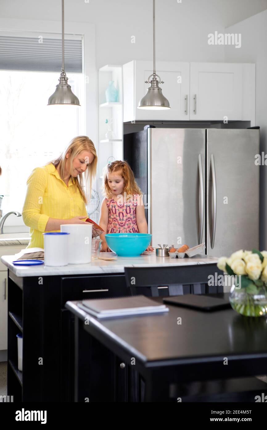 A mom and her toddler daughter baking together in a modern kitchen. Stock Photo