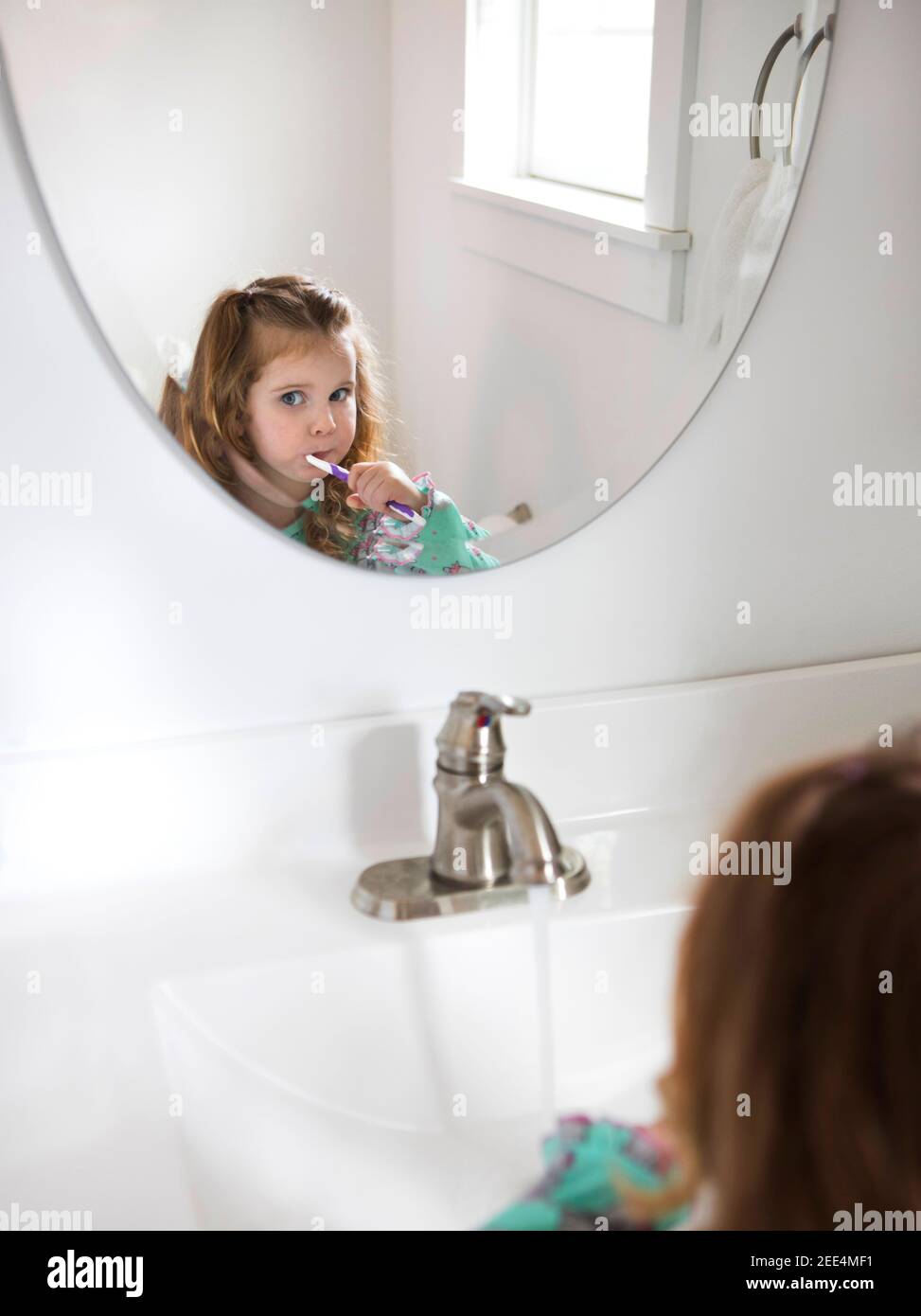 A little girl brushes her teeth in the bathroom mirror. Stock Photo