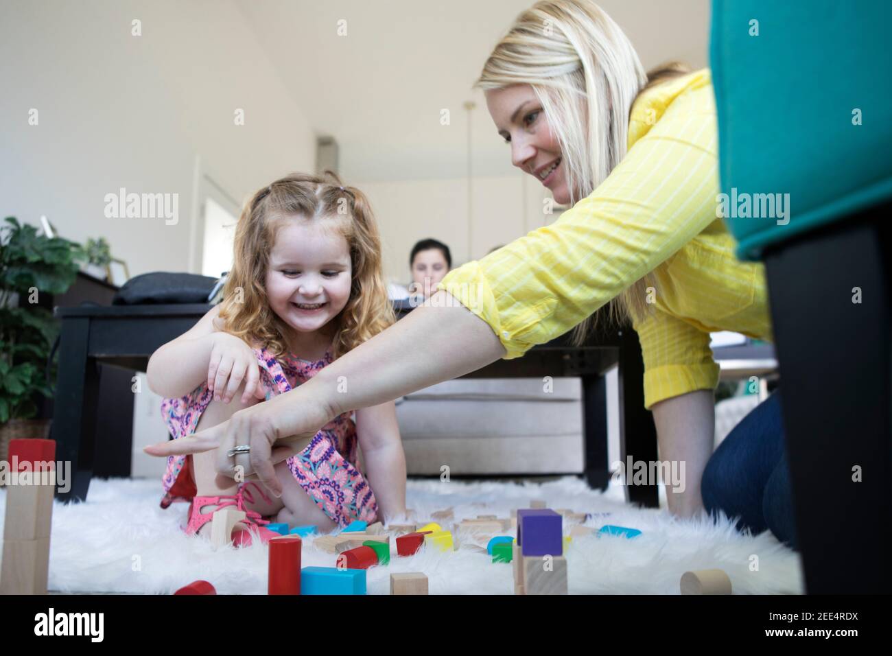 A mom or caregiver plays with a little girl on the floor of a modern home. Stock Photo