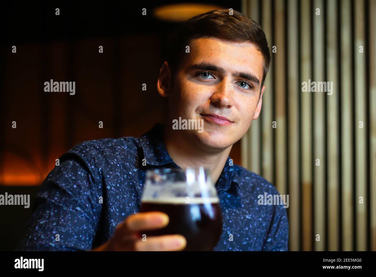 Handsome caucasian brown-haired young man holding glass of beer in restaurant. People, drinks, alcohol and leisure concept - happy young man drinking Stock Photo