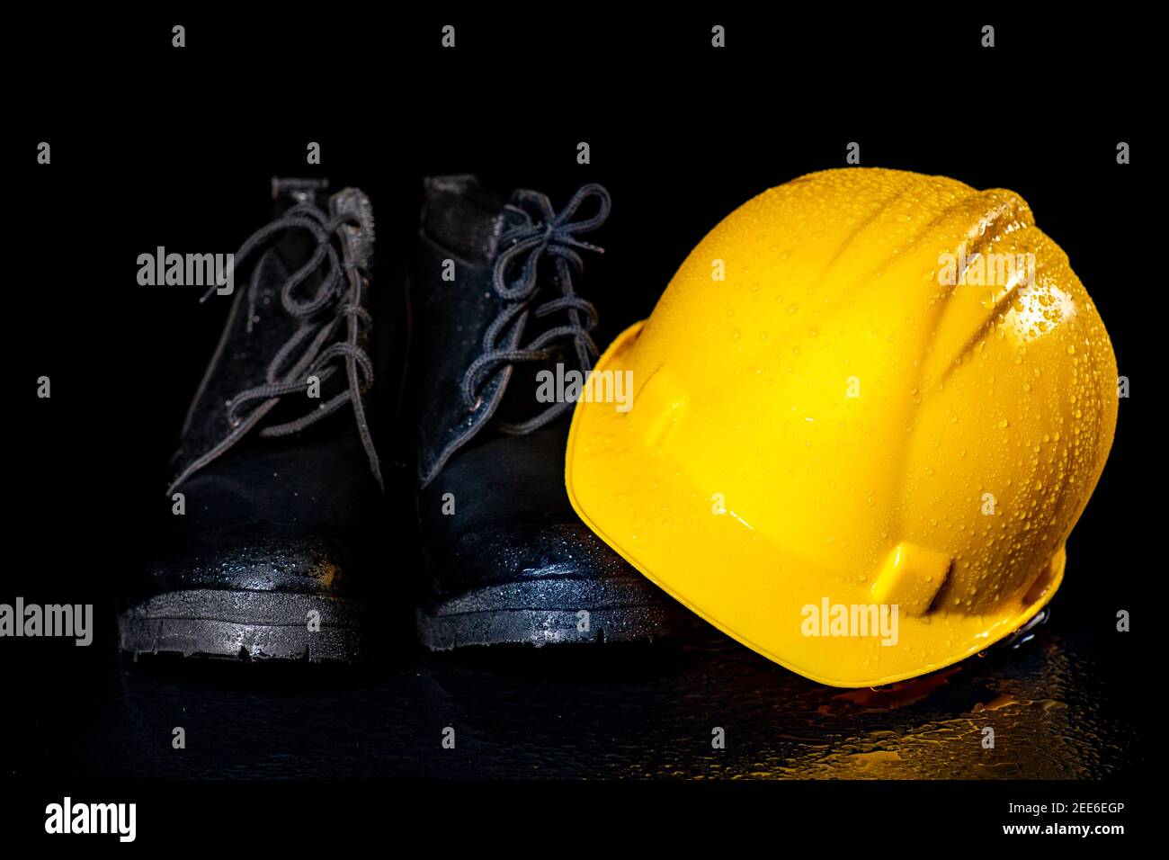 Black wet work boots and helmet on a dark table. Protective accessories for construction workers. Dark background. Stock Photo