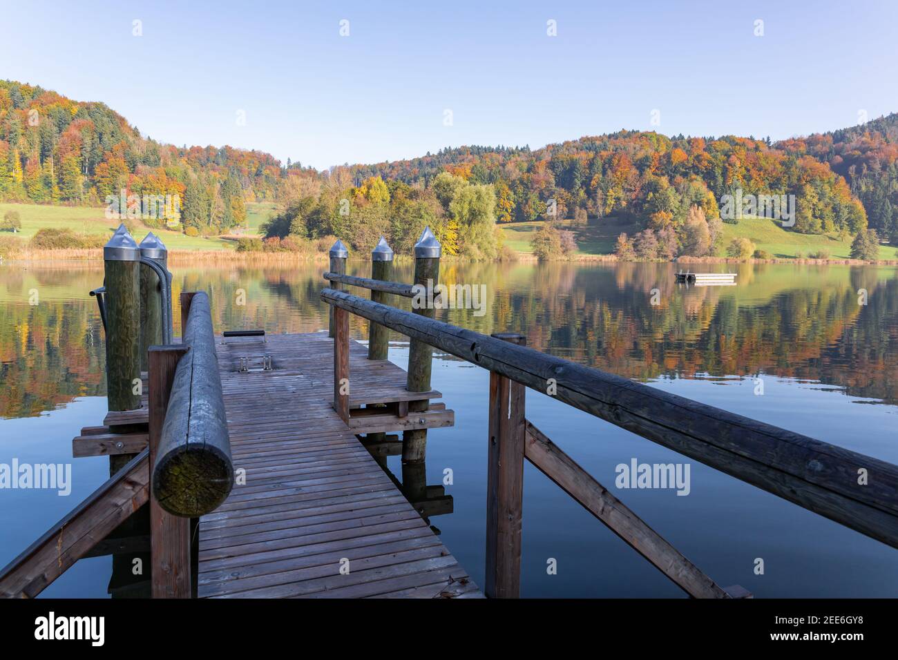 interesting brown wooden pier on the shore which is shaded, public bathing place, blue lake in autumn forest in the background, in the morning with br Stock Photo