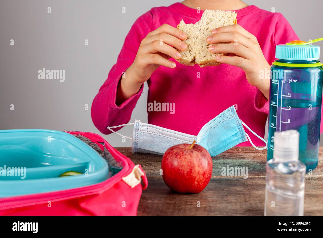 Closeup image with eating lunch at school concept during the phased reopening after COVID-19 pandemic closures. Girl with face mask removed eats sandw Stock Photo