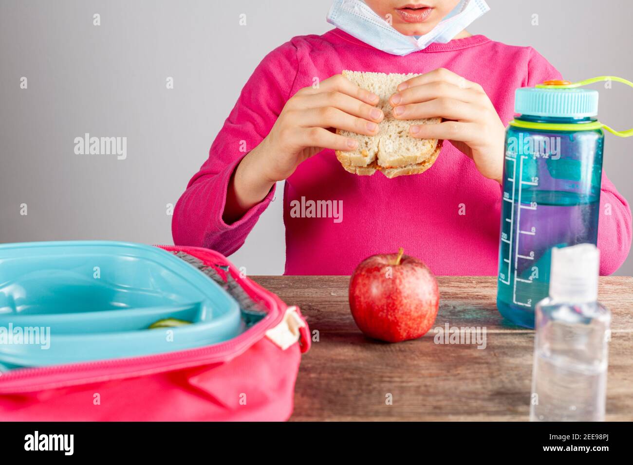 Closeup image with eating lunch at school concept during the phased reopening after COVID-19 pandemic closures. Girl with face mask removed eats sandw Stock Photo