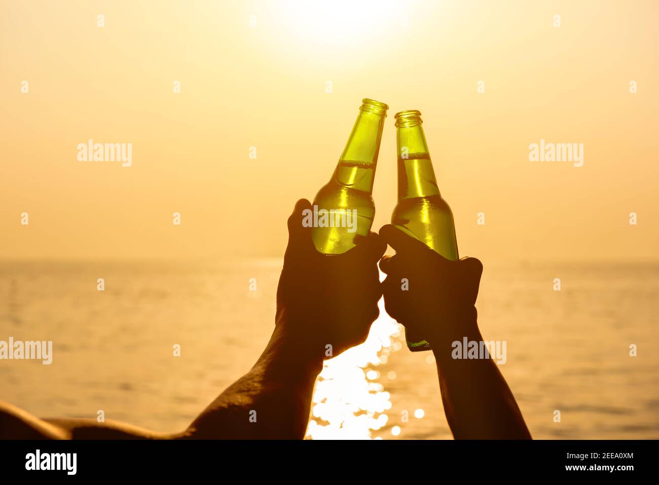 Couple hands holding beer bottles clanging and celebrating on holiday at the beach in summer sunset Stock Photo