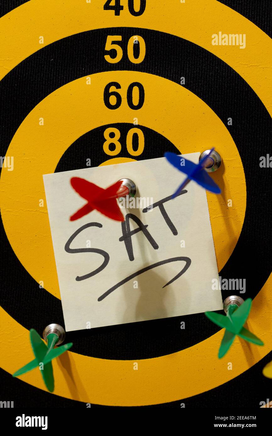 A dart board with multiple arrows. The red arrow hits the bullseye. A note that says SAT is underneath the winning arrrow. University Entrance, test p Stock Photo