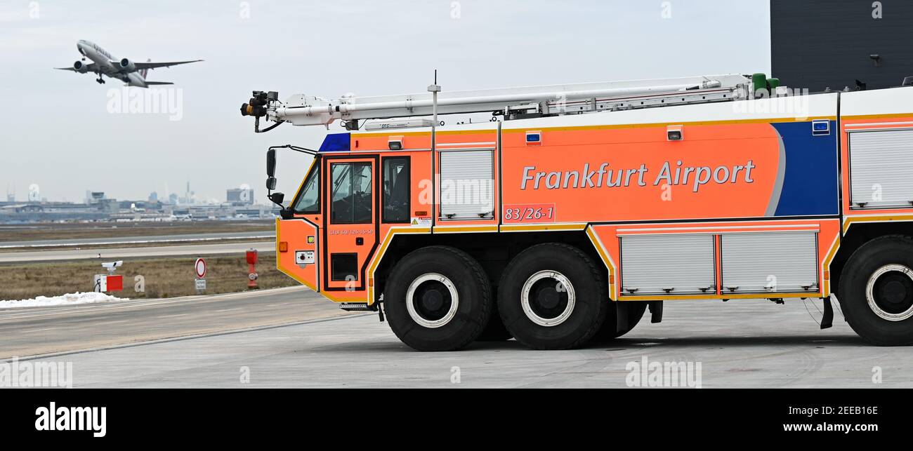 15 February 2021, Hessen, Frankfurt/Main: A Rosenbauer GFLF 60/125-15-5P Simba large airport fire engine stands on the grounds of the new Fire Station 1 in Frankfurt Airport's Cargo City South, while a passenger aircraft takes off. After a construction period of almost two and a half years, the new fire station has started operations. The building complex extends over a site of around 2.1 hectares. The new building combines numerous functions under one roof: in addition to the fire station, there is also a training center, preventive fire protection, administration and workshops. (to dpa 'Read Stock Photo