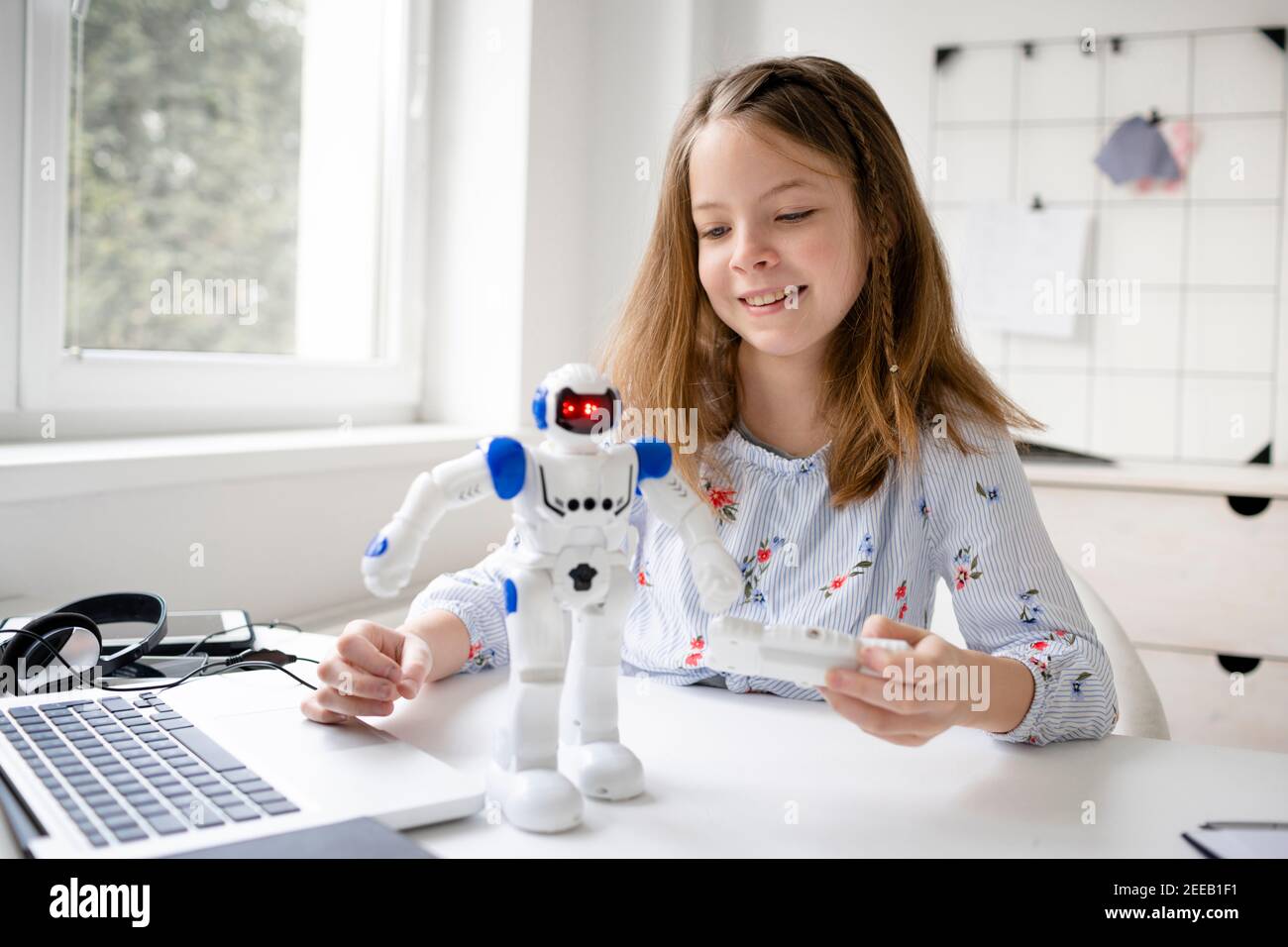 young, blond schoolgirl is playing with her robot toy and is having fun ...