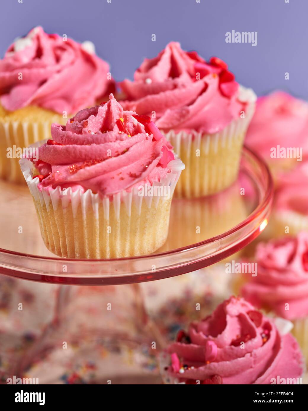 A display of bright pint frosted cupcakes sit on a clear pink cake