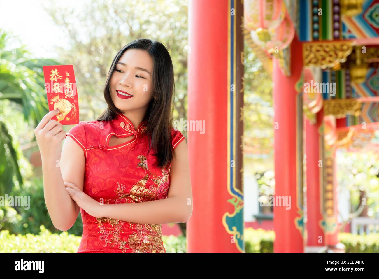 Smiling Asian woman in traditional red cheongsam qipao dress showing Chinese New Year greeting text sign said 'be rich and wealthy' Stock Photo