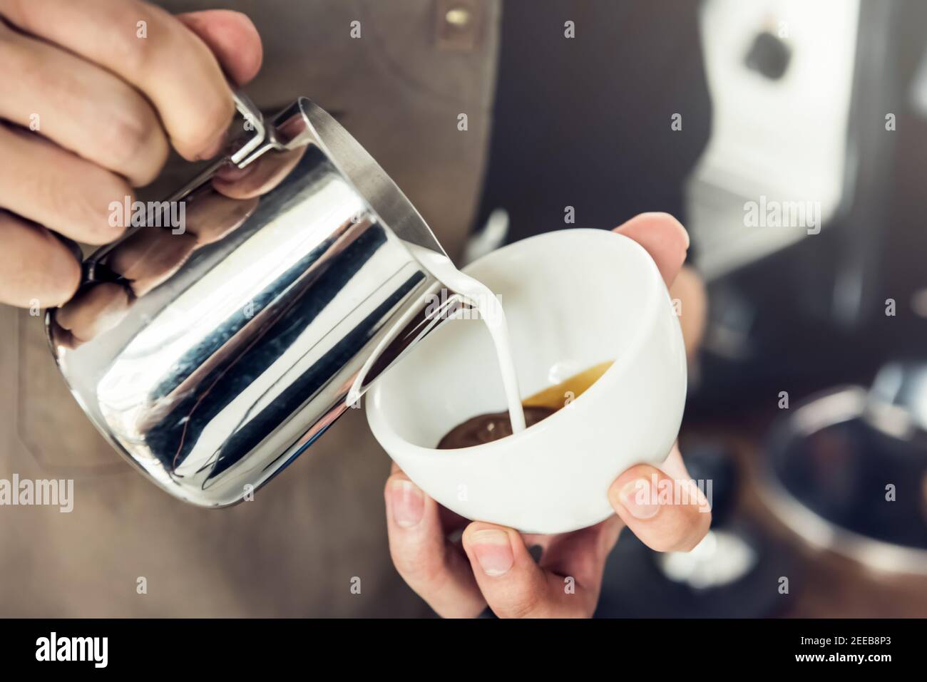 Professional barista pouring steamed milk into coffee cup making latte art Stock Photo