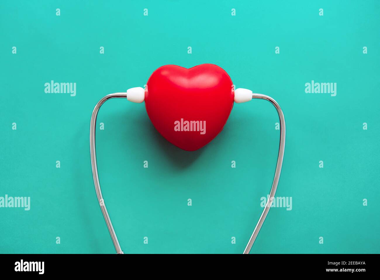 Red heart shape ball wearing stethoscope on green background, health care and medical concepts Stock Photo