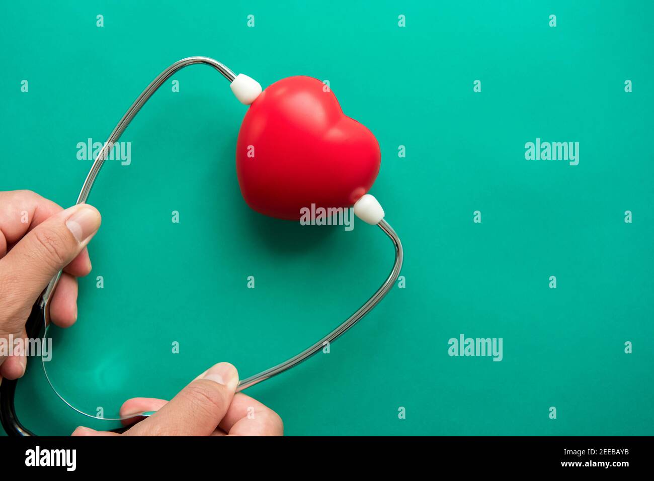 Red heart shape ball wearing stethoscope on green background, health care and medical concepts Stock Photo