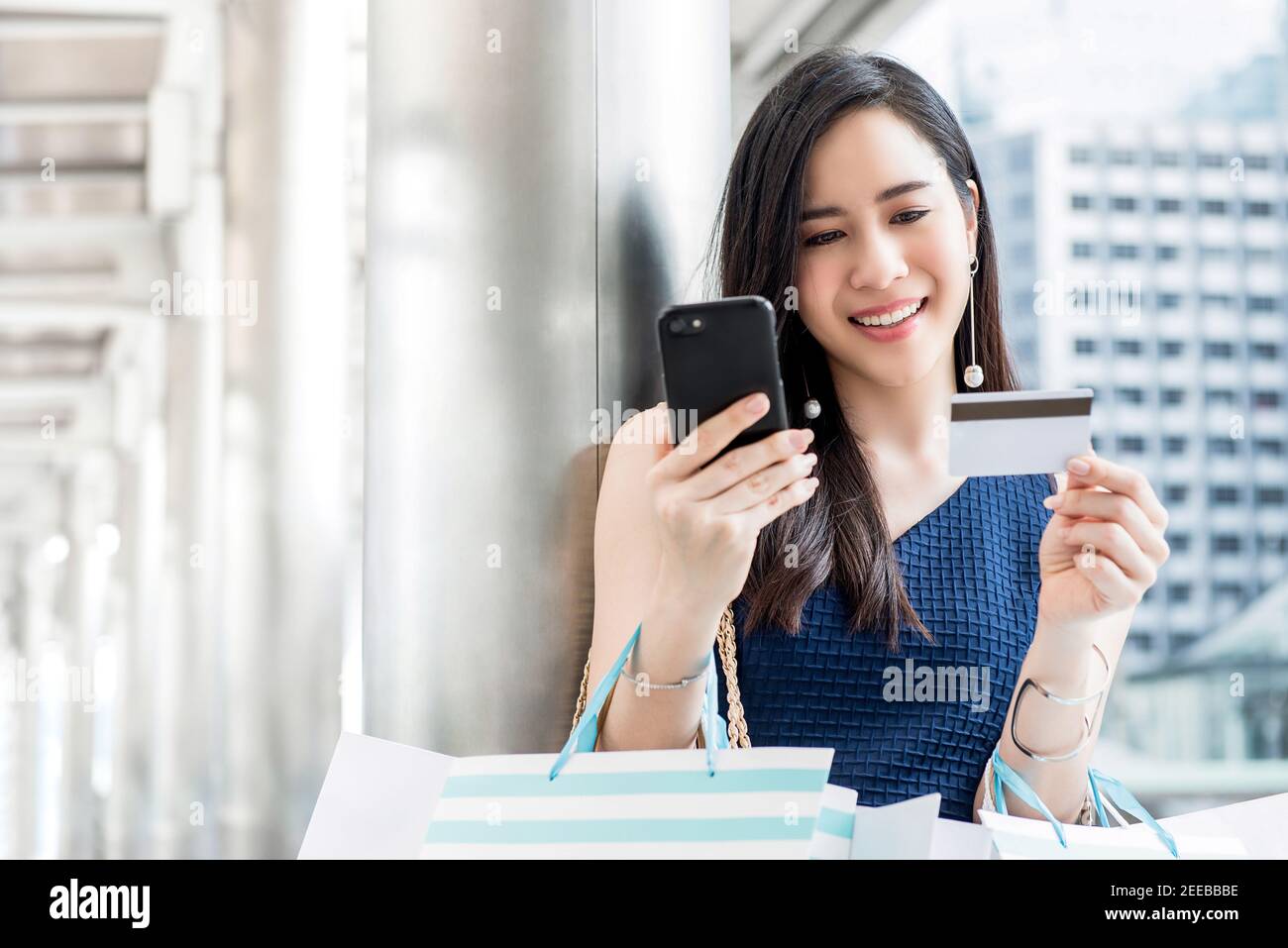 Beautiful young Asian woman making payment digitally with credit card after shopping online using mobile phone application technology Stock Photo