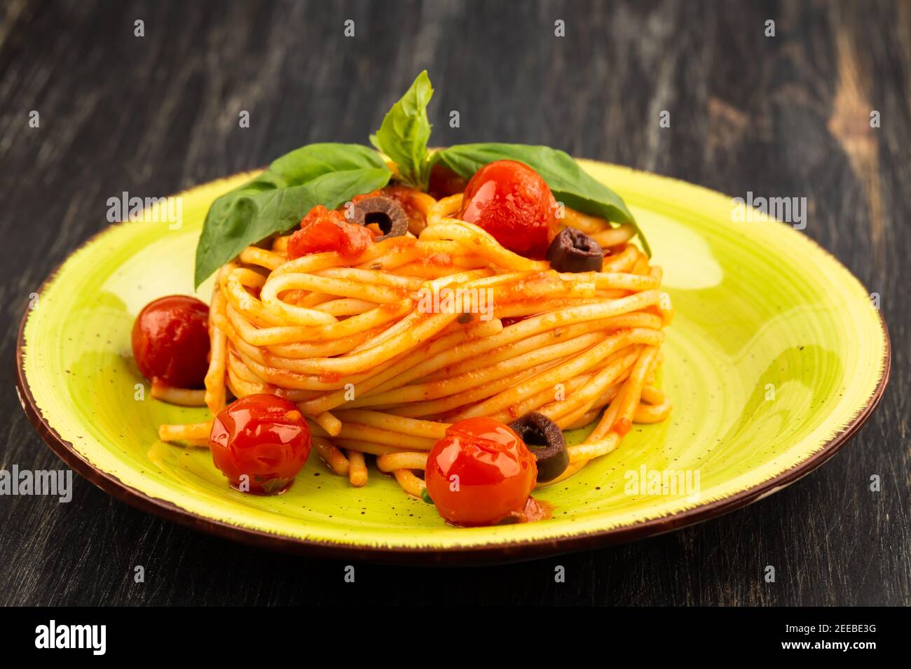 Pasta spaghetti Napoli or Napolitana on green plate on black background. Italian cuisine. Stock Photo