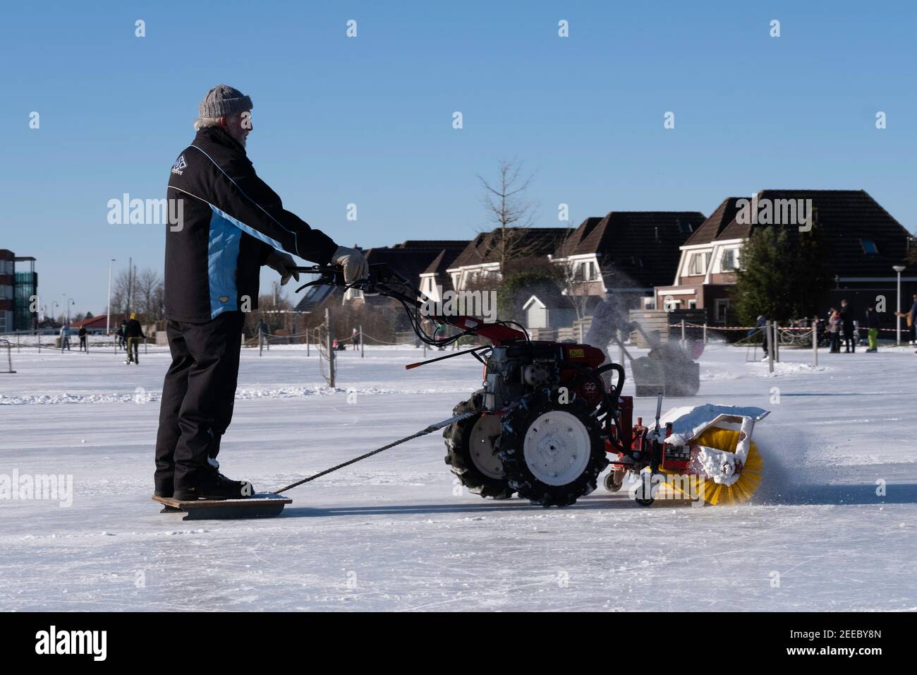 Man cleans the ice rink in winter snow with a sweeper and a snow blower. He can be pulled on a