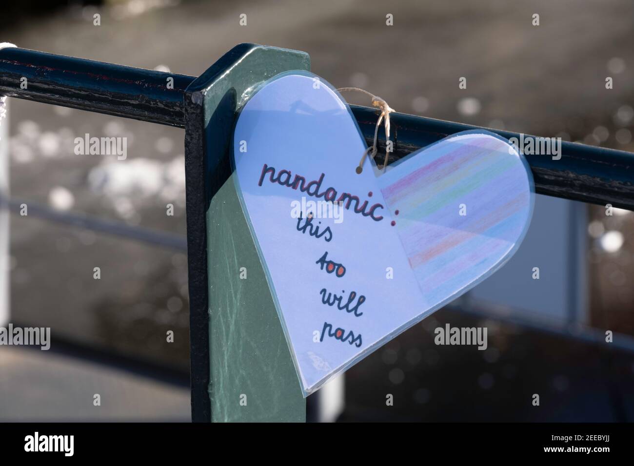 Plasticized paper heart with handwritten text 'Pandamic: this too will pass' hangs from the railing of a bridge in Lemmer, the Netherlands Stock Photo