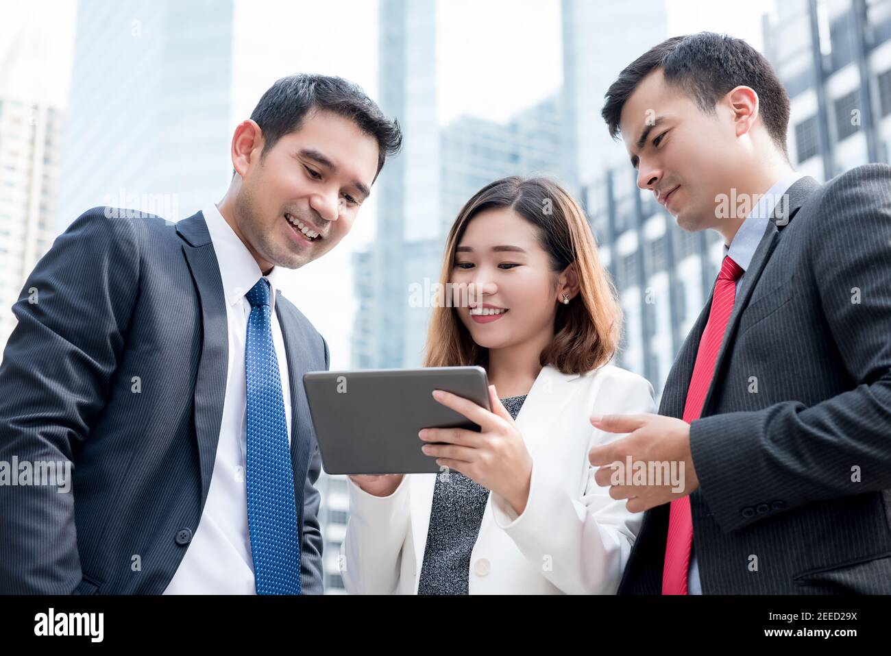 Group of multiethnic business team discussing work on tablet computer outdoors in the city Stock Photo