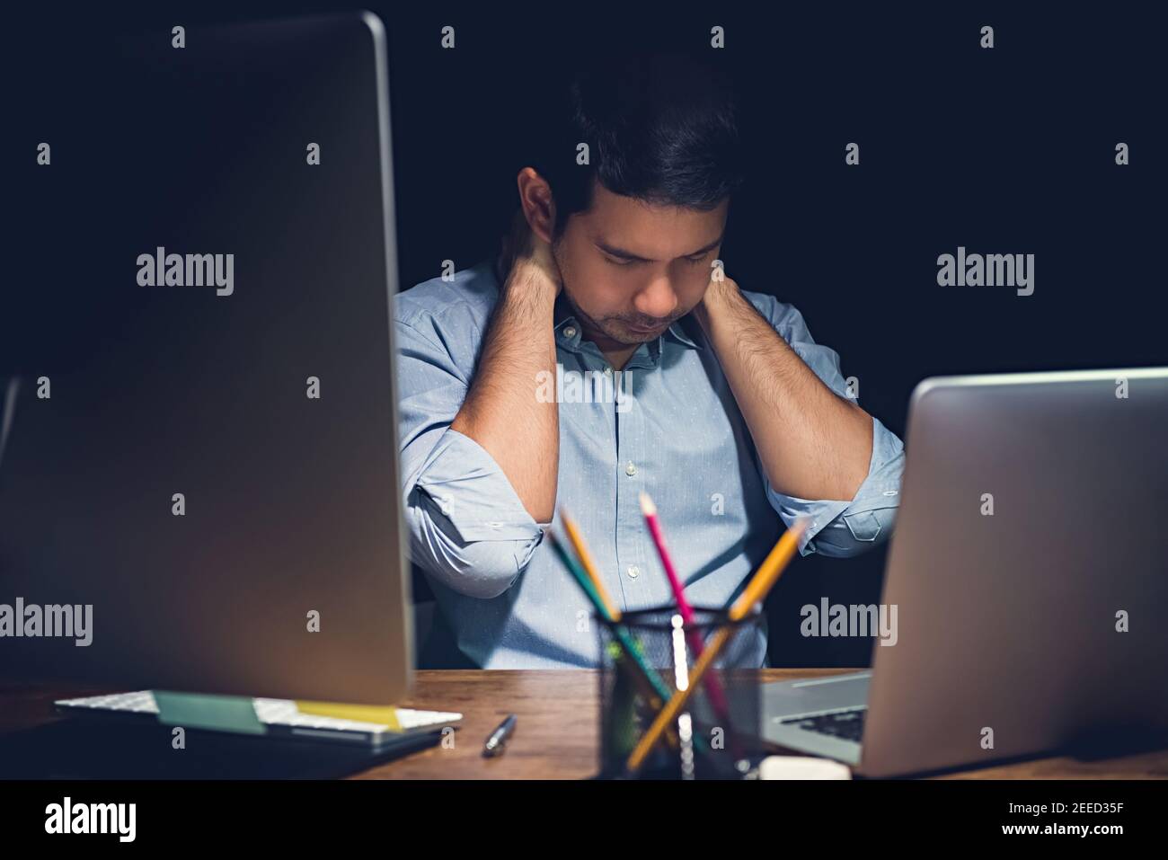Stressed tired young man having office syndrome , neck pain, while working overtime on his laptop computer at night finishing his project Stock Photo