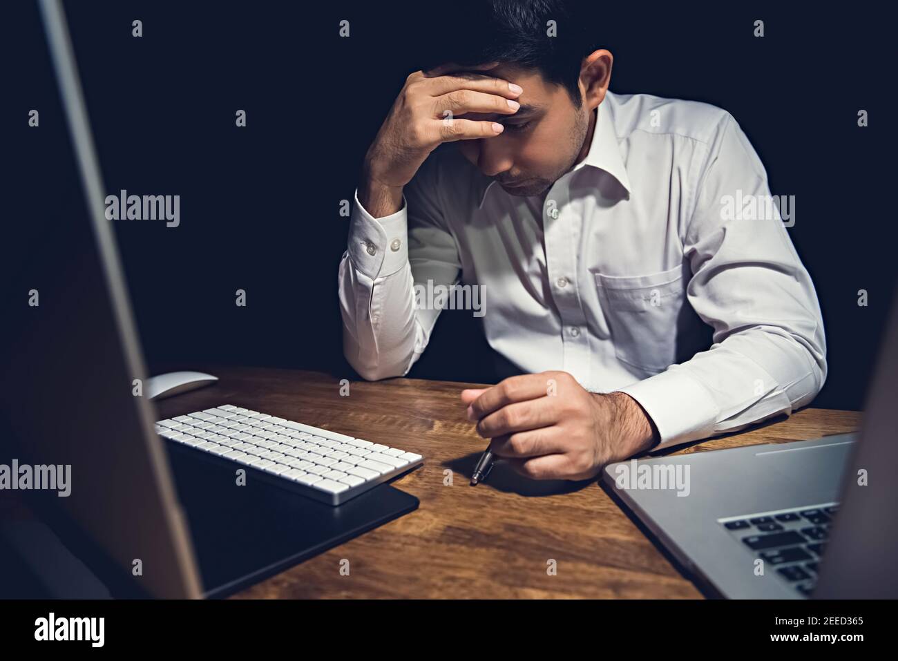 Stressed tired young man feeling headache while working overtime on his laptop computer at night finishing his project Stock Photo