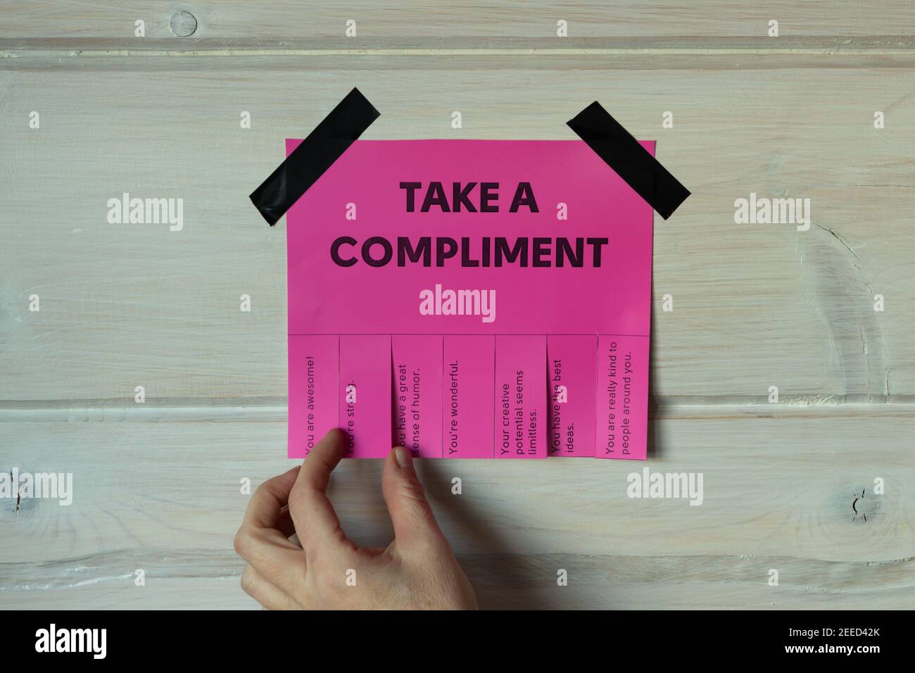 Happy World Compliment Day. Take a compliment. Pink wall paper sticker with text of popular compliments for beautiful lady pasted on wooden background Stock Photo