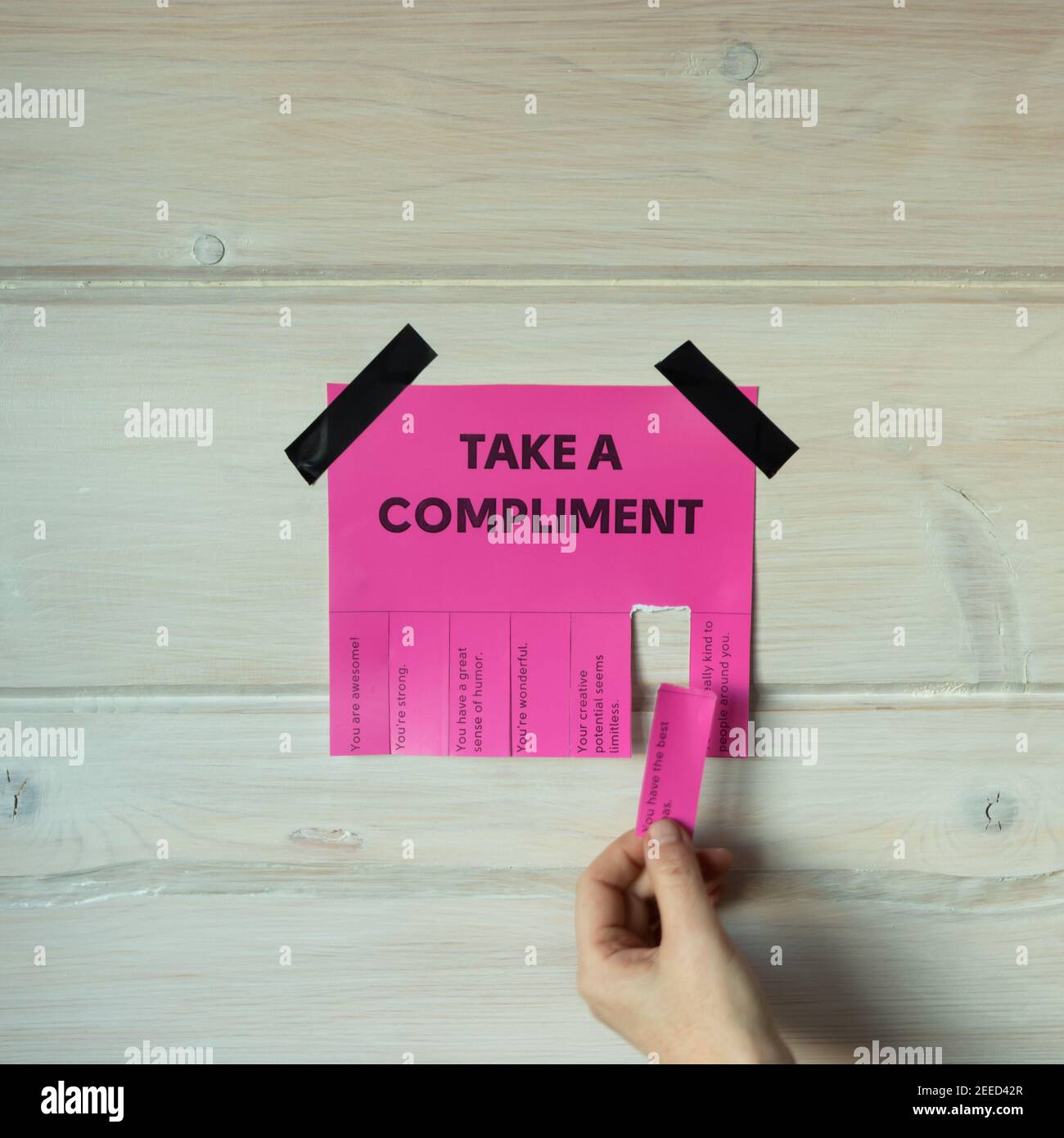 Happy World Compliment Day. Take a compliment. Pink wall paper sticker with text of popular compliments for beautiful lady pasted on wooden background Stock Photo