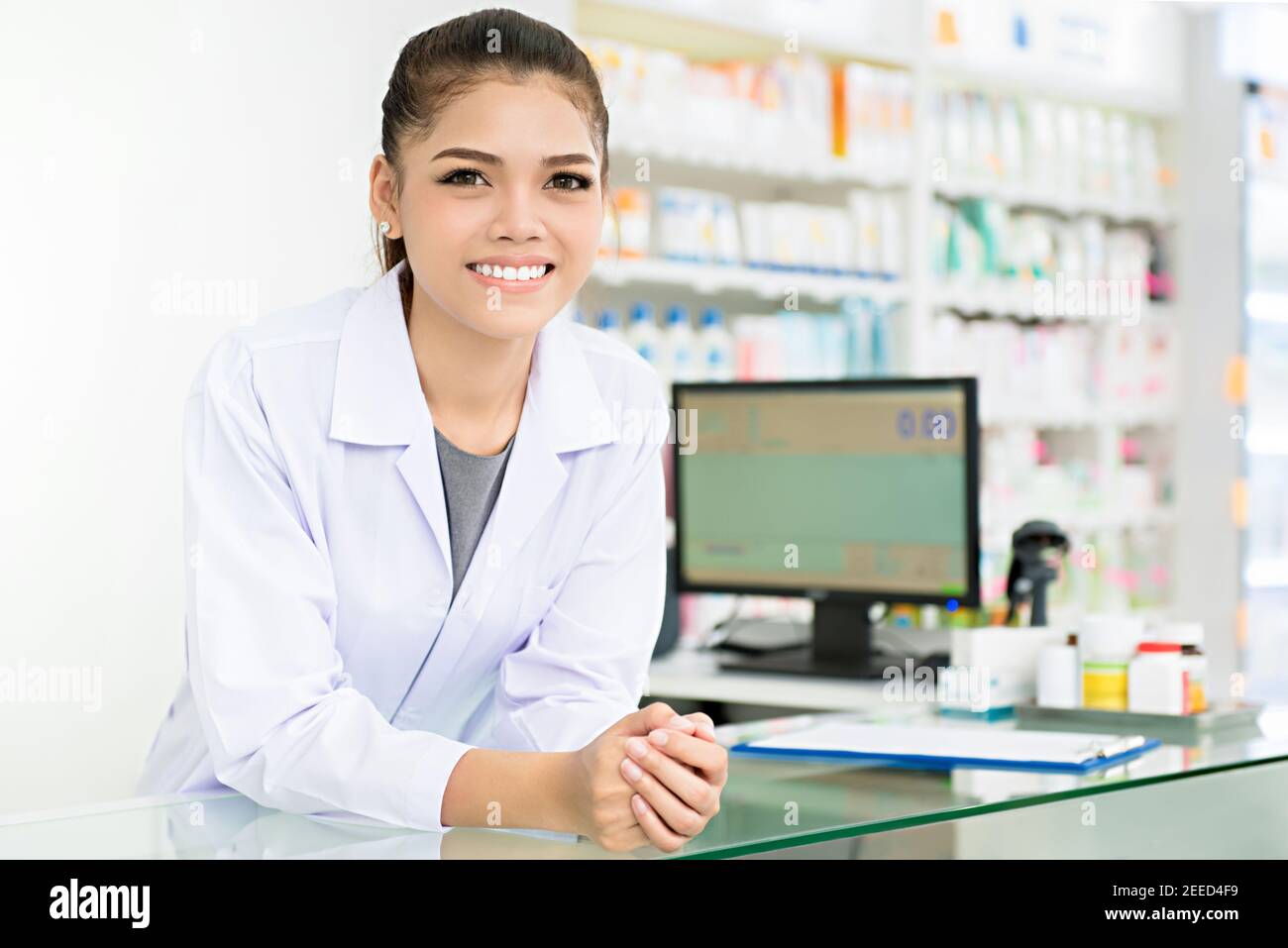 Smiling beautiful young Asian woman pharmacist in white gown coat at the counter in pharmacy (chemist shop or drugstore) Stock Photo