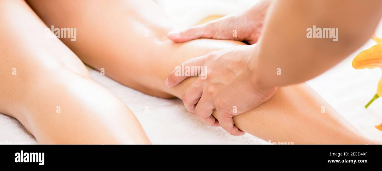 Professional therapist giving relaxing reflexology Thai oil leg massage treatment to a woman in spa - panoramic banner Stock Photo