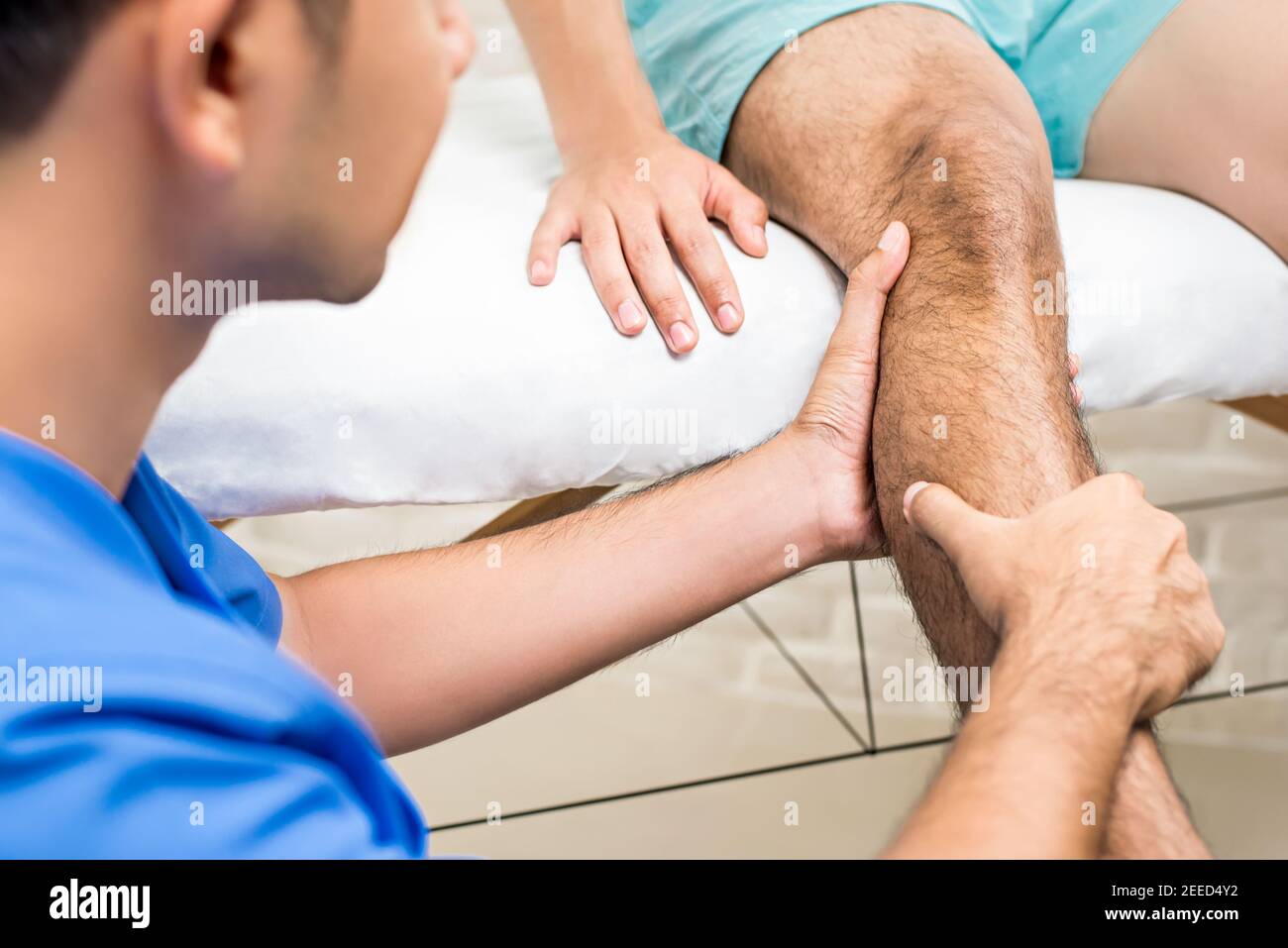 Doctor (therapist) treating male patient leg while sitting on the bed in clinic - physical therapy concept Stock Photo