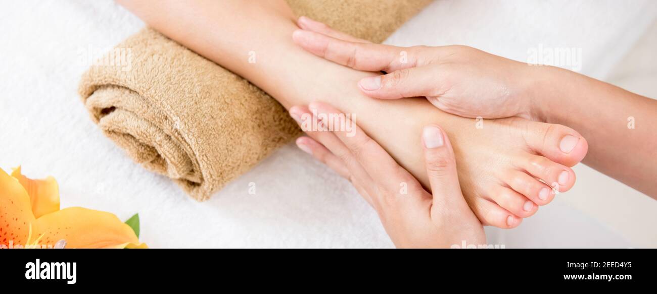 Professional therapist giving relaxing reflexology Thai foot massage treatment to a woman in spa - panoramic banner Stock Photo