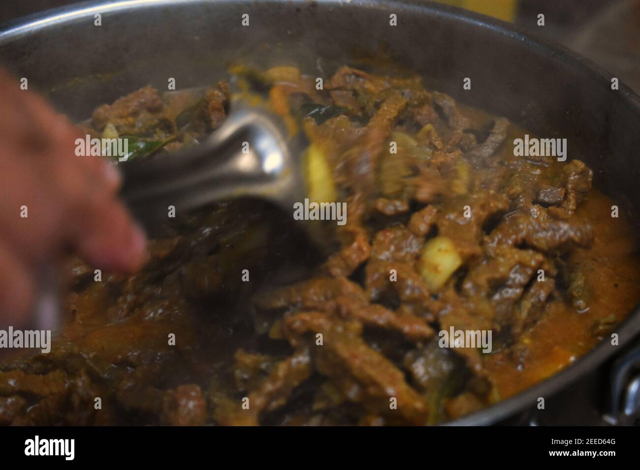 a pot of beef curry from Kerala India cooking on stove with someone