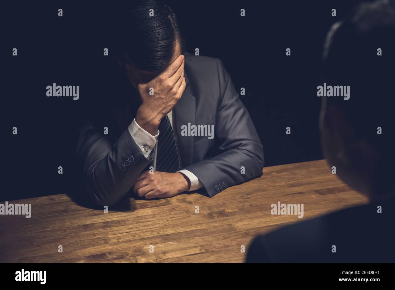 Suspect businessman displaying regret, worry and concern using body language in dark interrogation room Stock Photo