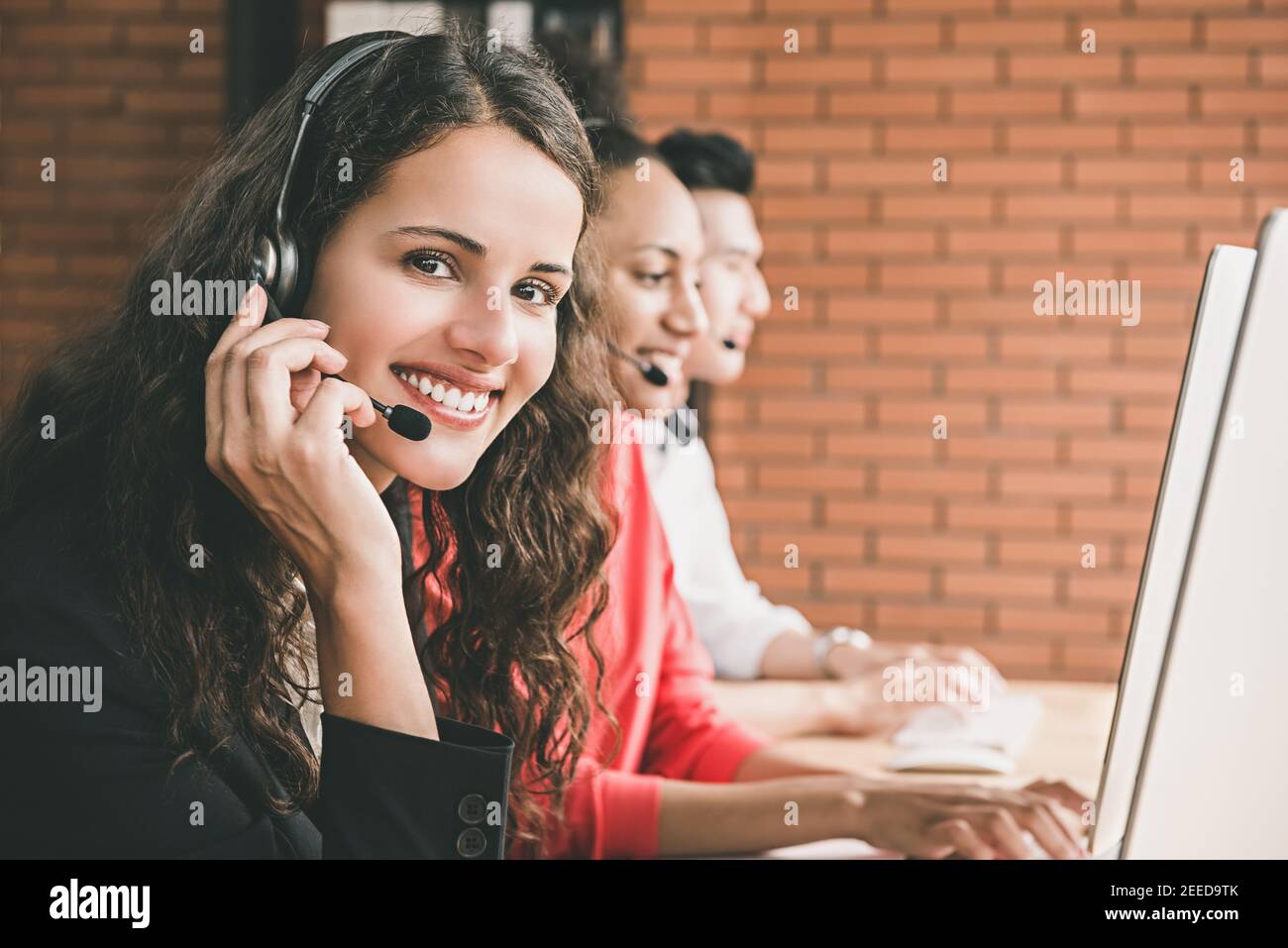 Smiling beautiful woman telemarketing customer service agent working in call center office with her multiethnic team Stock Photo