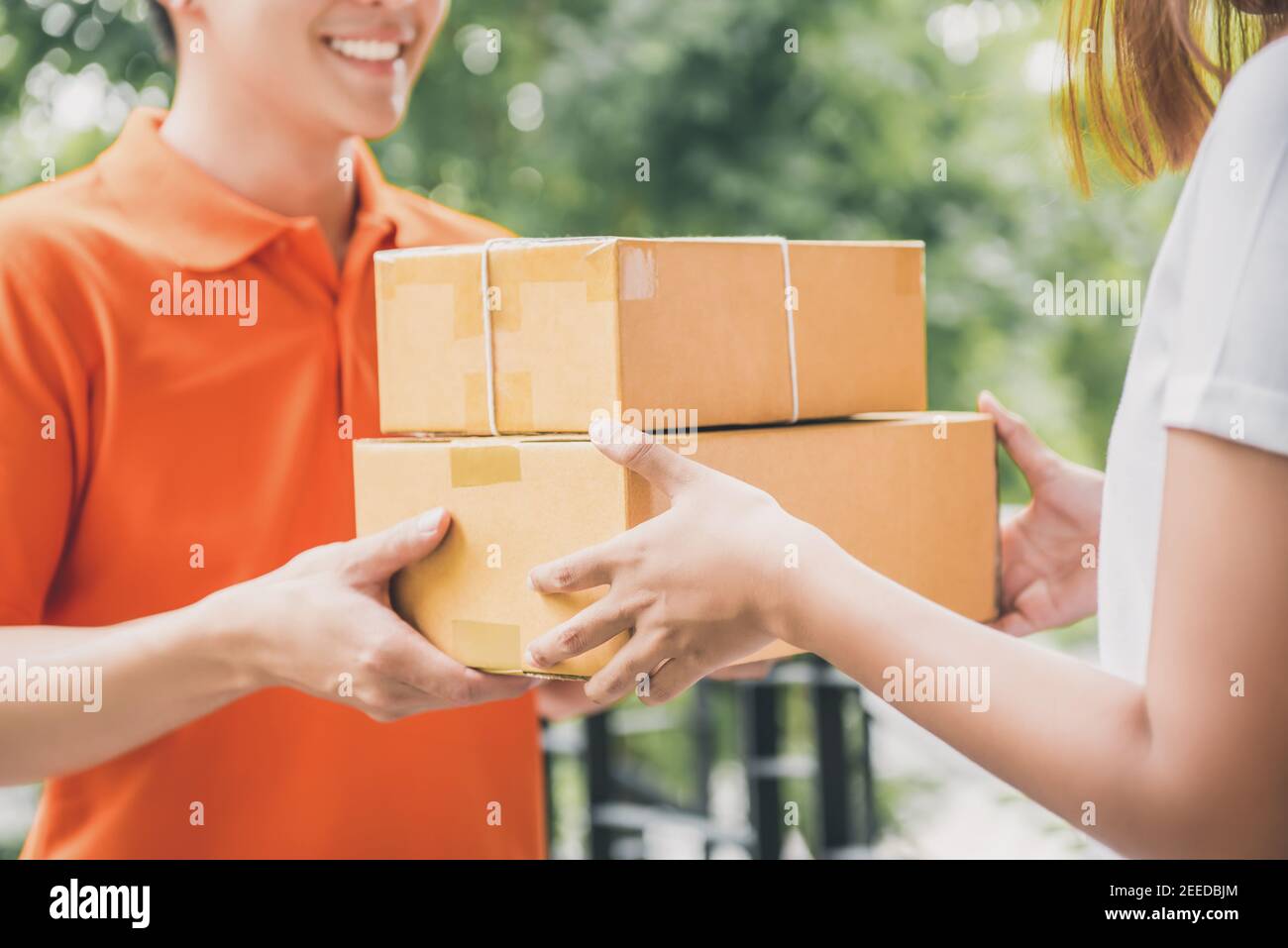 Smiling delivery man in orange uniform delivering parcel box to a woman customer - courier service concept Stock Photo