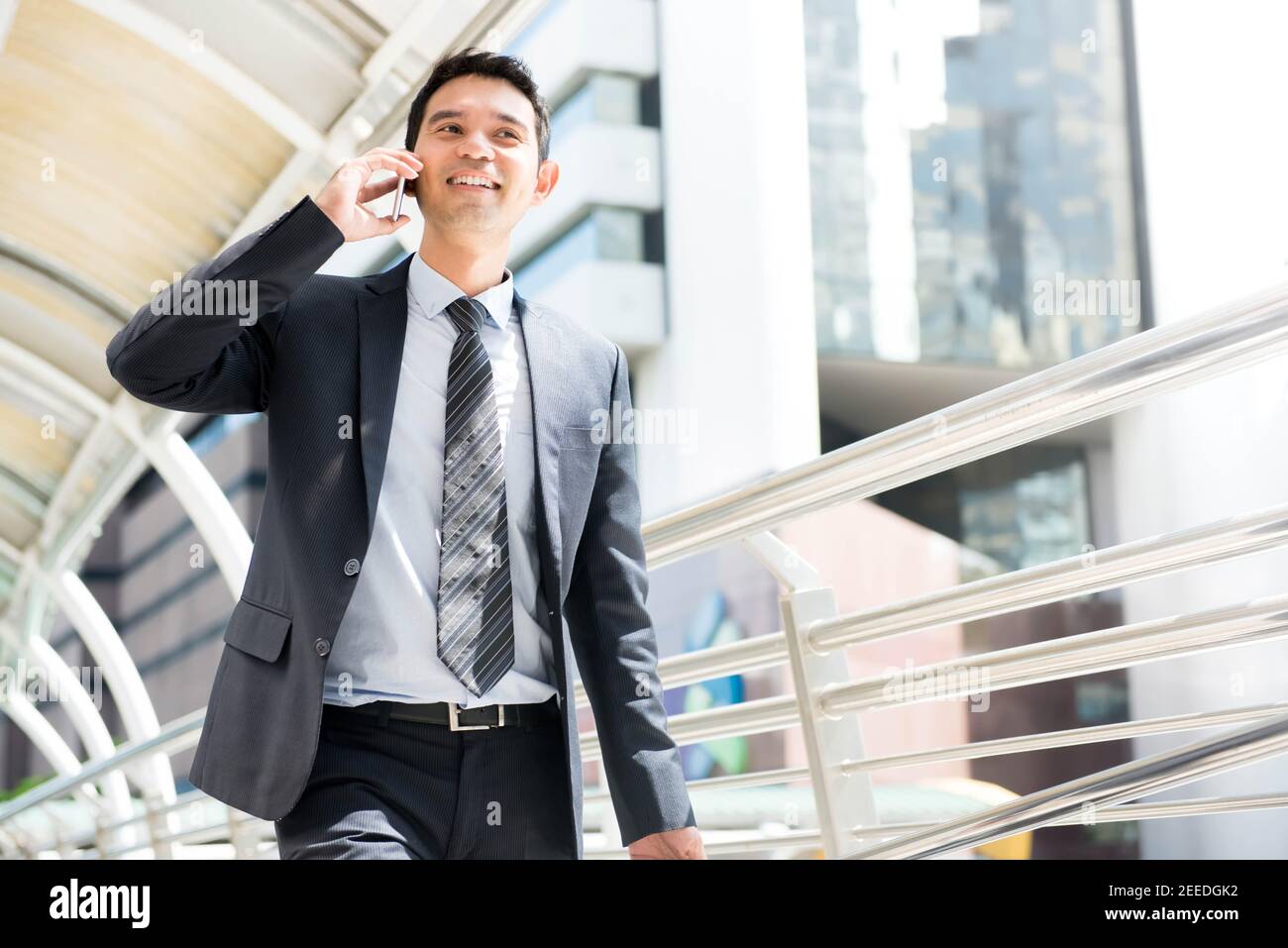 Enthusiastic Thai-Asian Business man walking while talking on mobile phone in the city on the way to work at the office Stock Photo