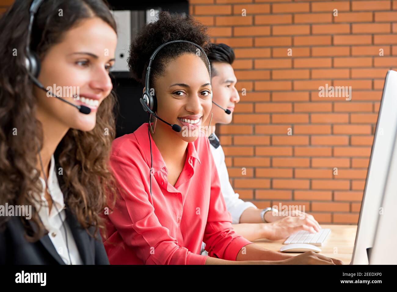 Smiling black female telemarketing customer service agent working in call center with multi-ethnic team Stock Photo