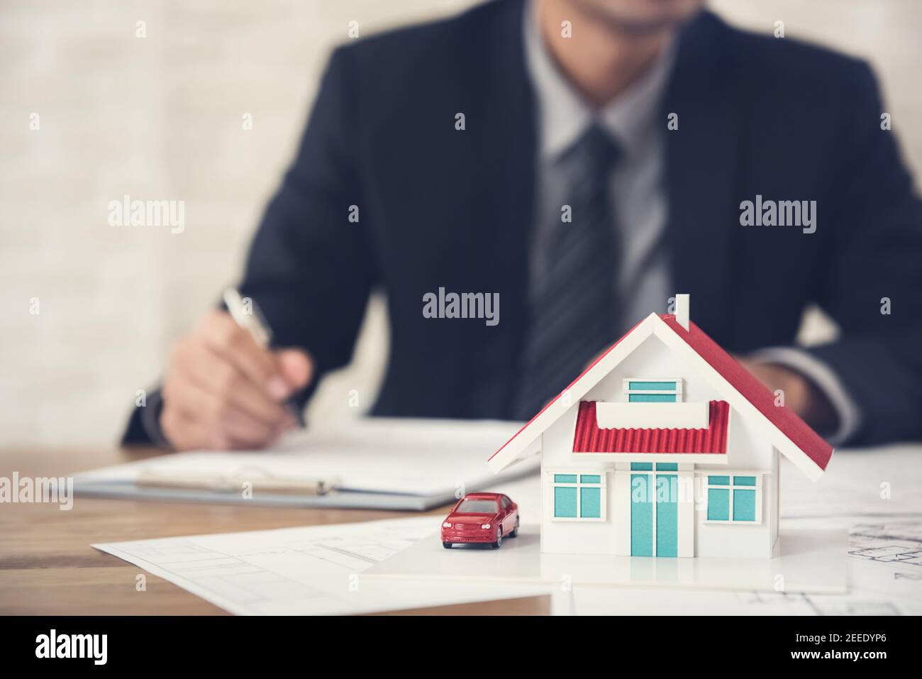 Real estate agent signing document with house model and blueprint on