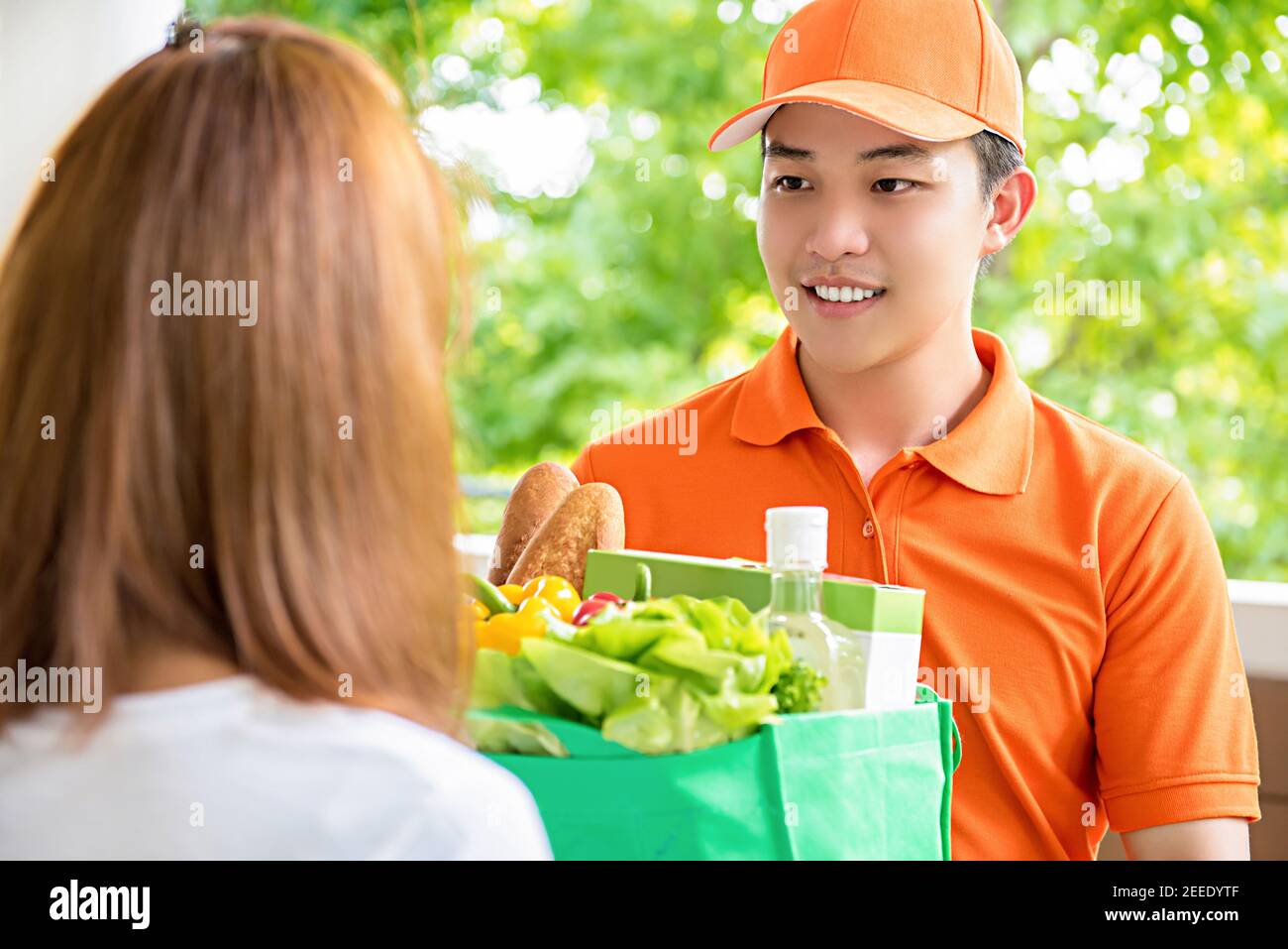 Asian delivery man delivering food to a woman at home - online grocery shopping service concept Stock Photo