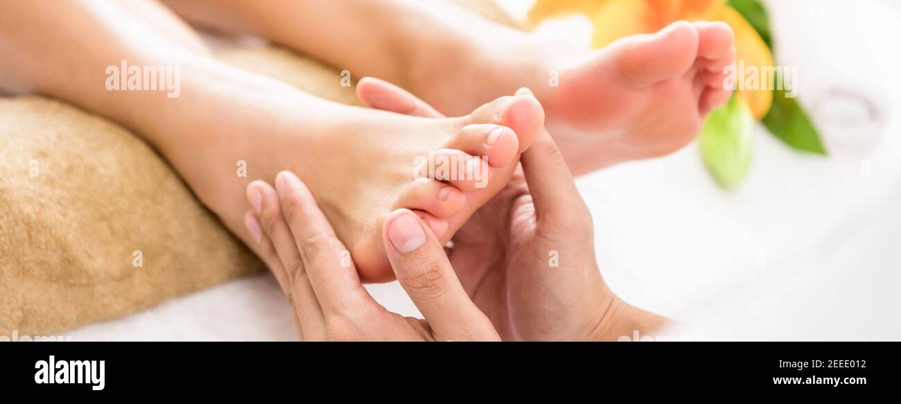 Professional therapist giving relaxing reflexology Thai foot massage to a woman in spa - horizontal web banner Stock Photo