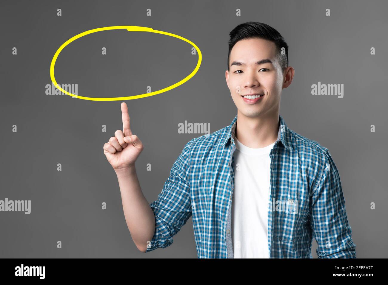 Cheerful smiling young Asian man pointing his finger up to empty circle - can put your texts inside Stock Photo