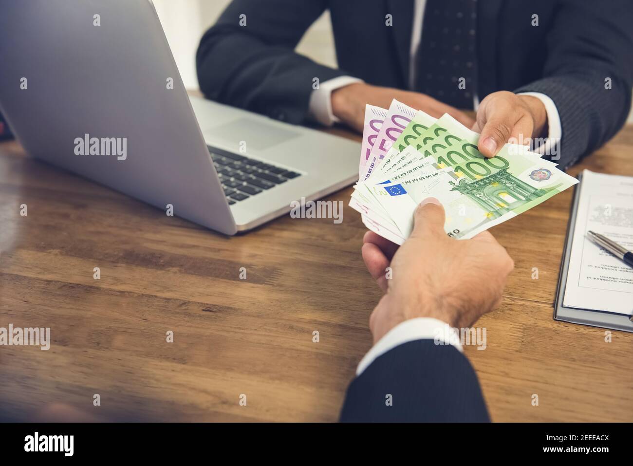 Businessman giving money, Euro banknotes, to his partner while making contract Stock Photo